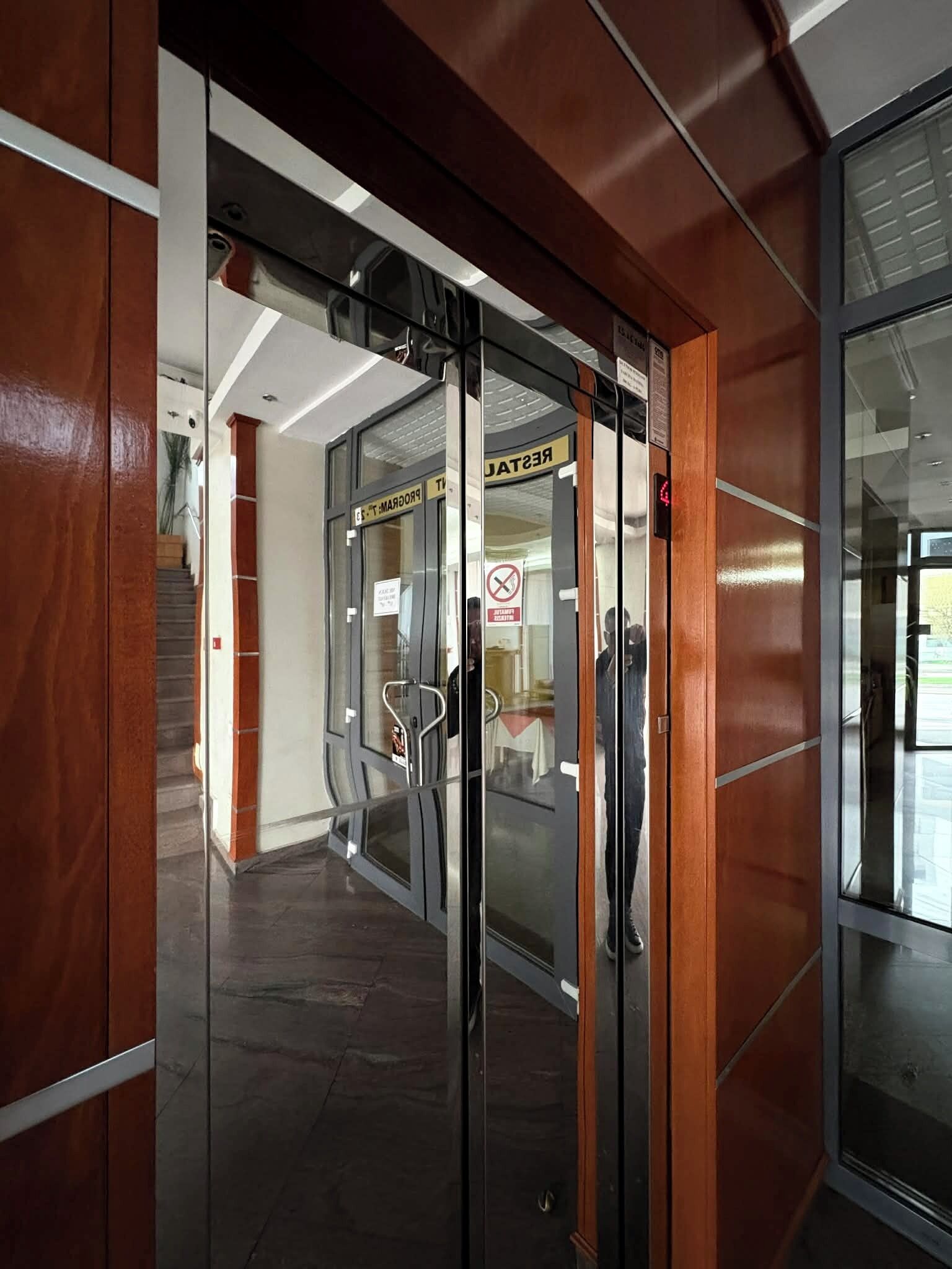A modern building entrance with glass doors, a staircase, and a sign indicating a restricted area.