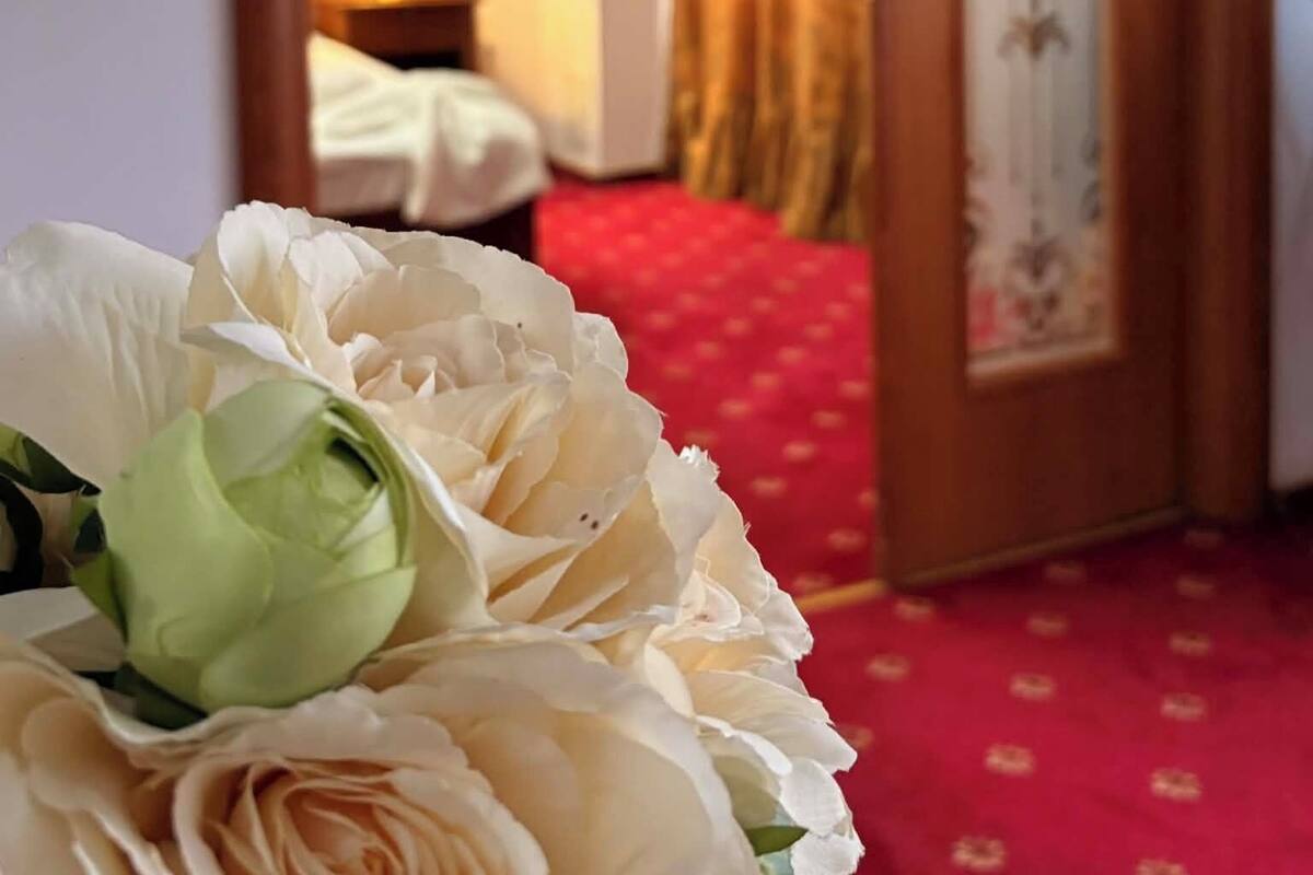 Hotellihuone, jossa on punainen matto, puinen ovi lasiruutuin ja valkoisella päällisellä varustettu sänky.