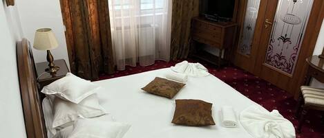 A hotel room with a bed, pillows, a TV, a lamp, a wardrobe, and a window with curtains.