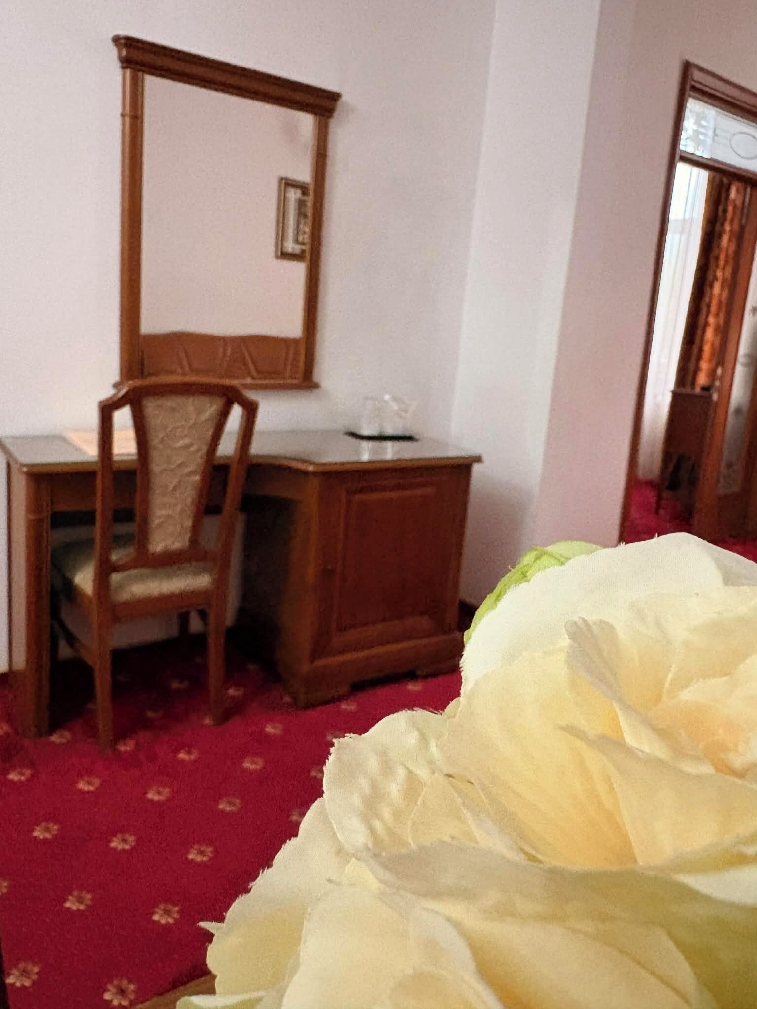 A room with a wooden desk, a chair, a mirror, and a bed with white bedding.