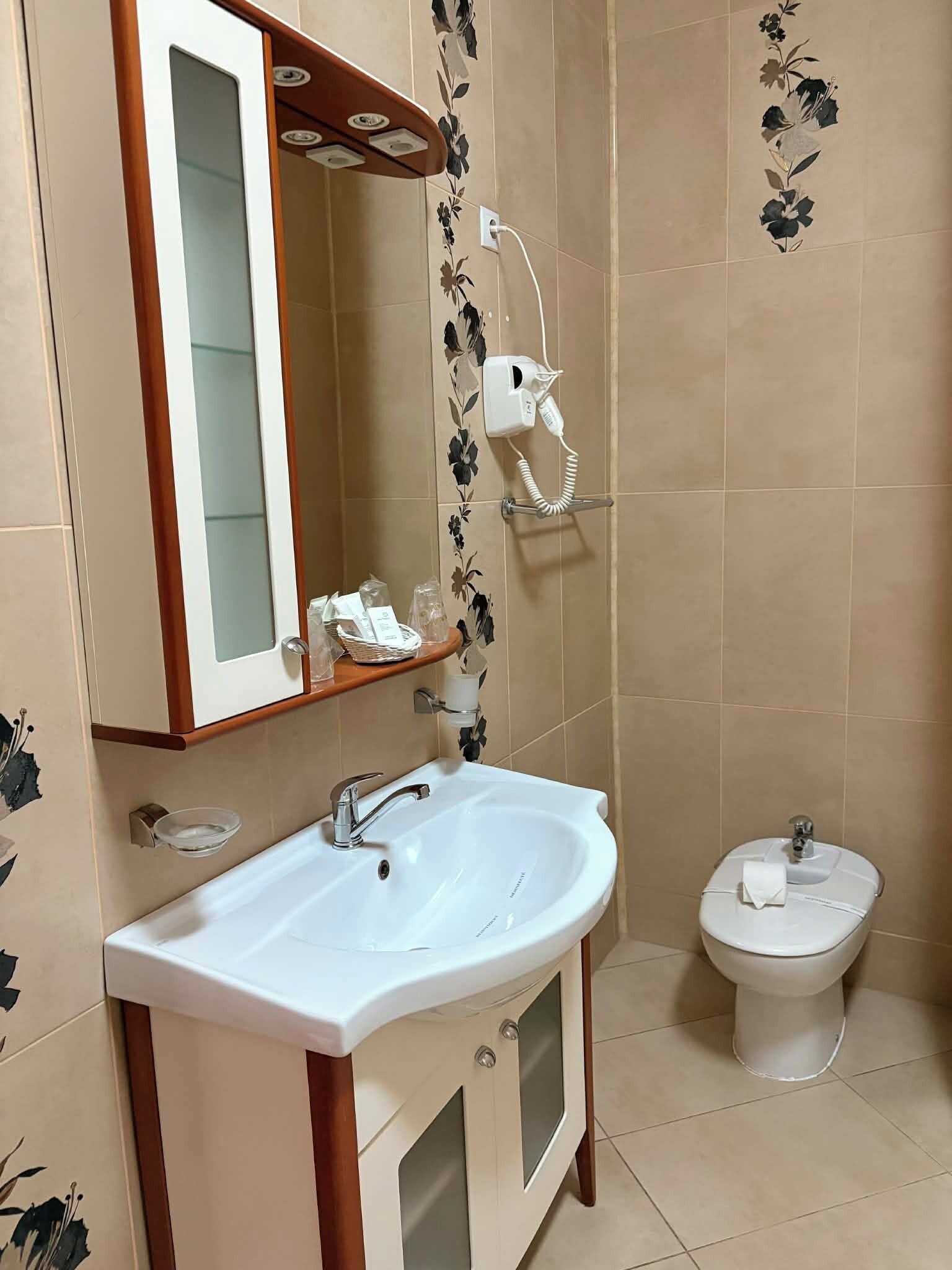 A bathroom with a white sink, a mirror, a toilet, and a hairdryer on the wall.