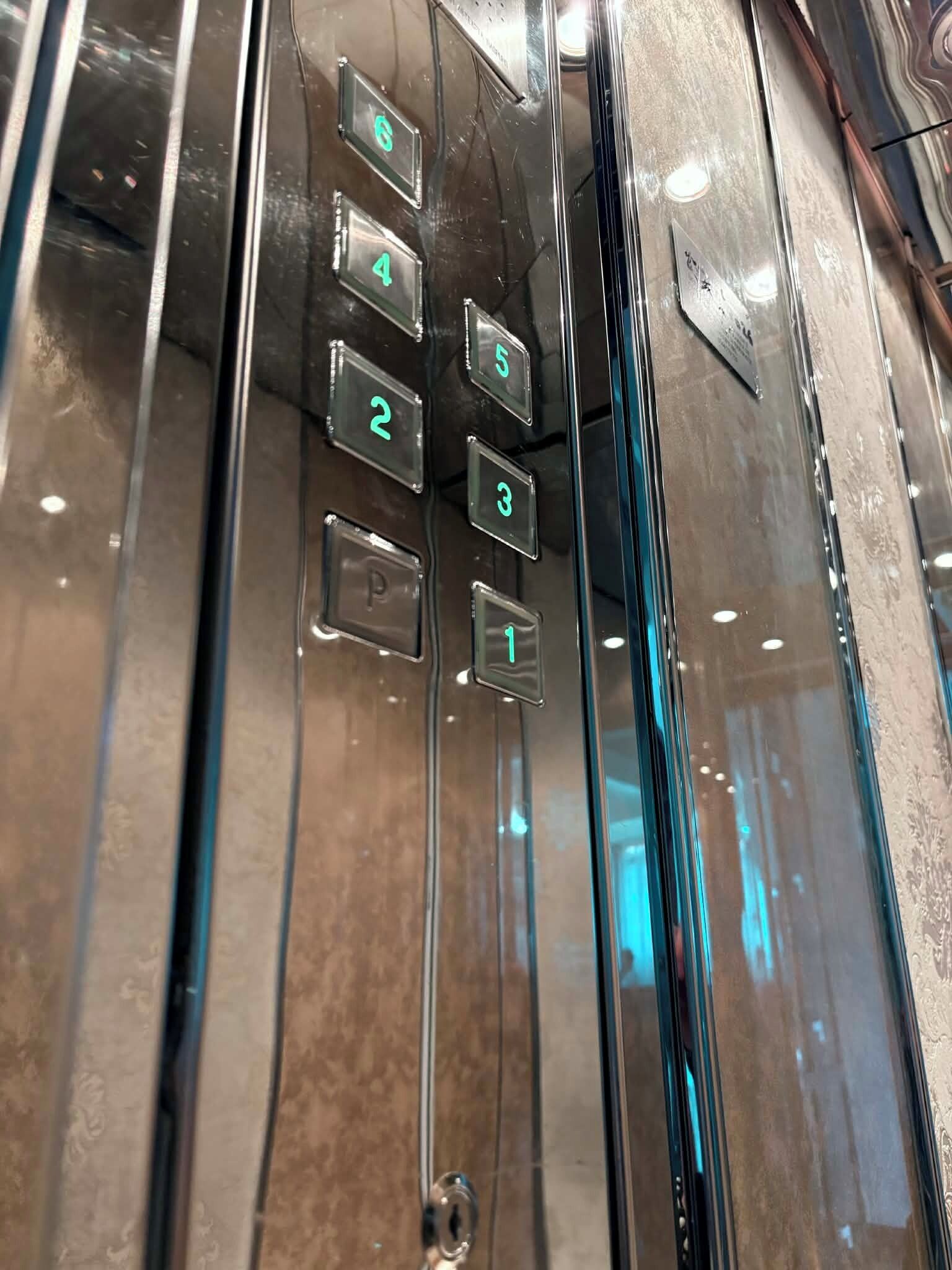Interior de un ascensor con paredes metálicas y una serie de botones numerados del 1 al 6.