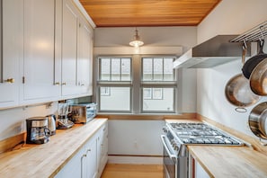 A kitchen with white cabinets, a stove, a coffee maker, and a window with blinds. - Steps to Montana State! Updated Bozeman Bungalow (Bozeman)