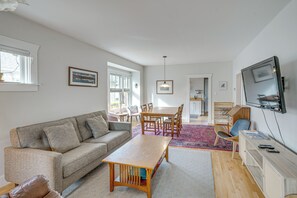 A living room with a sofa, coffee table, TV, and dining area with chairs and a table. - Steps to Montana State! Updated Bozeman Bungalow (Bozeman)