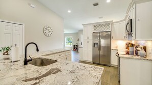 A kitchen with a sink, stainless steel refrigerator, white cabinets, and a clock on the wall. - Jump Into Fall at This Cozy Gem w/ Private Pool! (Palm Bay)