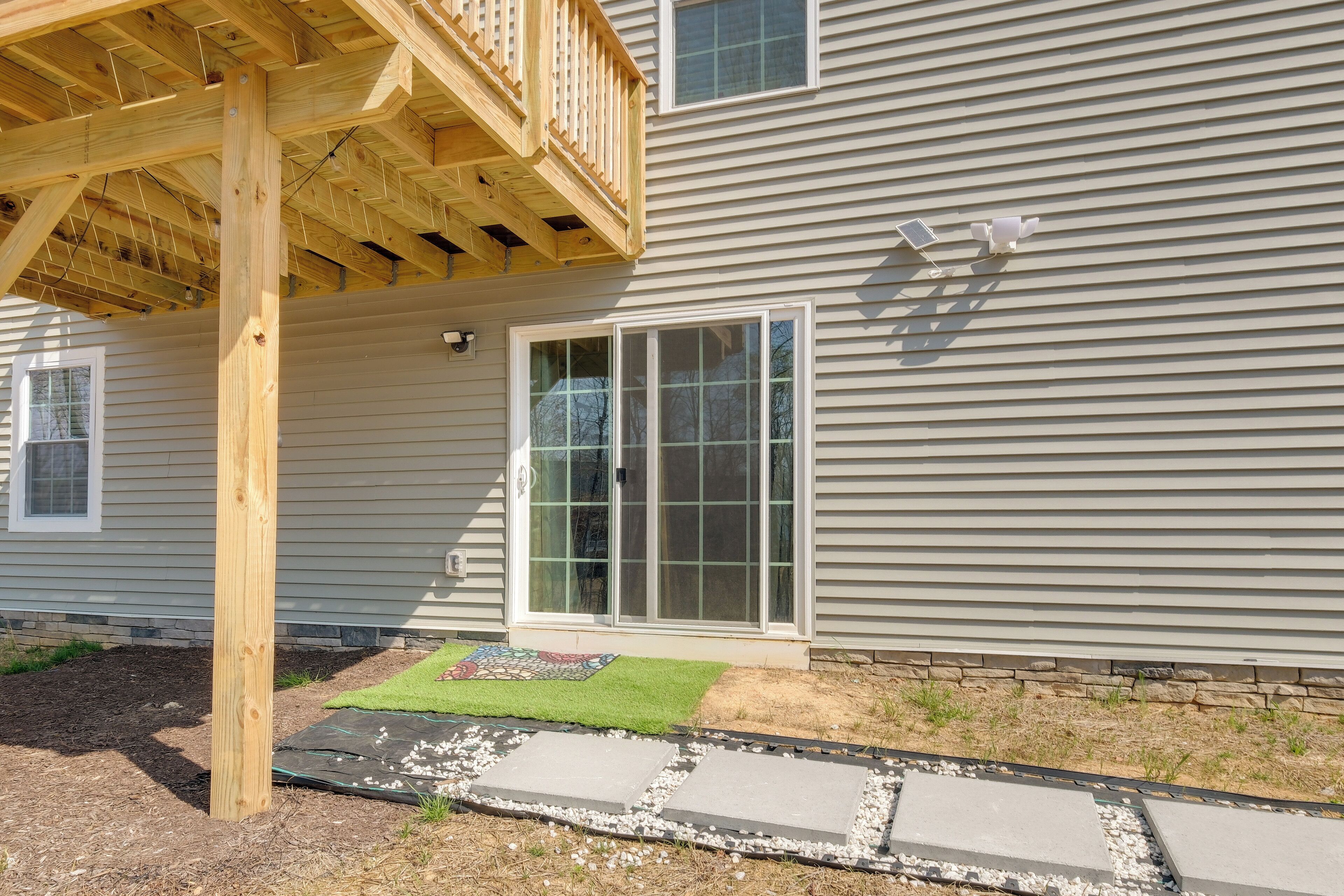 A house with a wooden deck, a large sliding glass door, and a stone pathway leading to the door.