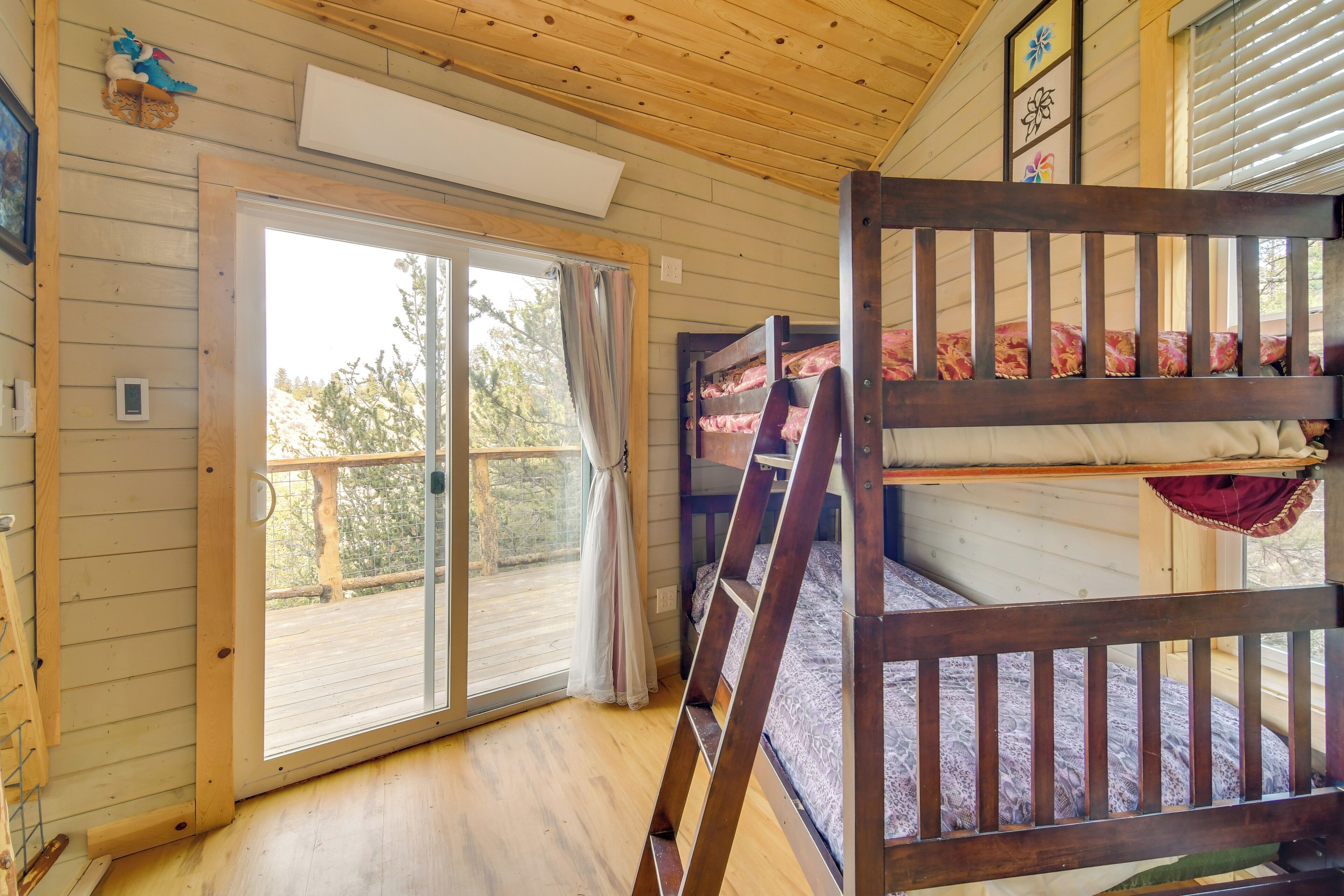 A wooden cabin interior with a sliding glass door leading to a deck, bunk beds, and a ladder.