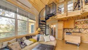 A cozy cabin interior with a wooden staircase, a sofa with cushions, and a kitchen area. - 'Mystic Treehouse' on 35 Acres Near Hartsel (Hartsel)