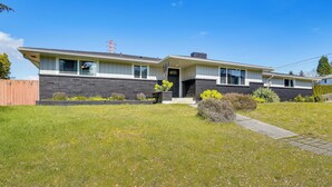 Kaksikerroksinen talo, jossa on etupiha, puinen aita ja kirkkaan sininen taivas.