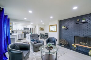 A modern living room with a glass coffee table, two leather armchairs, a fireplace, and a kitchen in the background. - 3 Mi to Point Defiance Park: Family Home w/ Yard! (Tacoma)