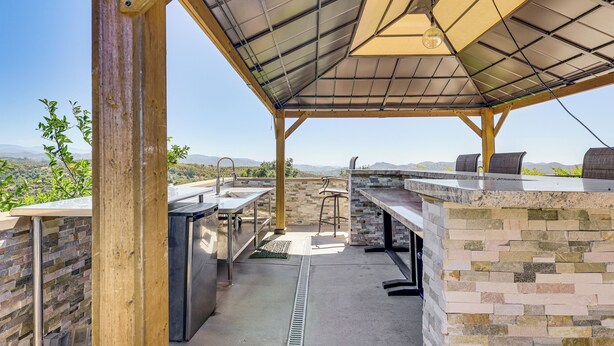 Une cuisine extérieure avec un mur en pierre, un barbecue et une vue sur les montagnes.