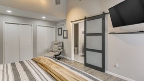 Ein Schlafzimmer mit einem Bett, einem Sessel, einer Schiebetür, einem Deckenventilator und einem Wand-Fernseher.