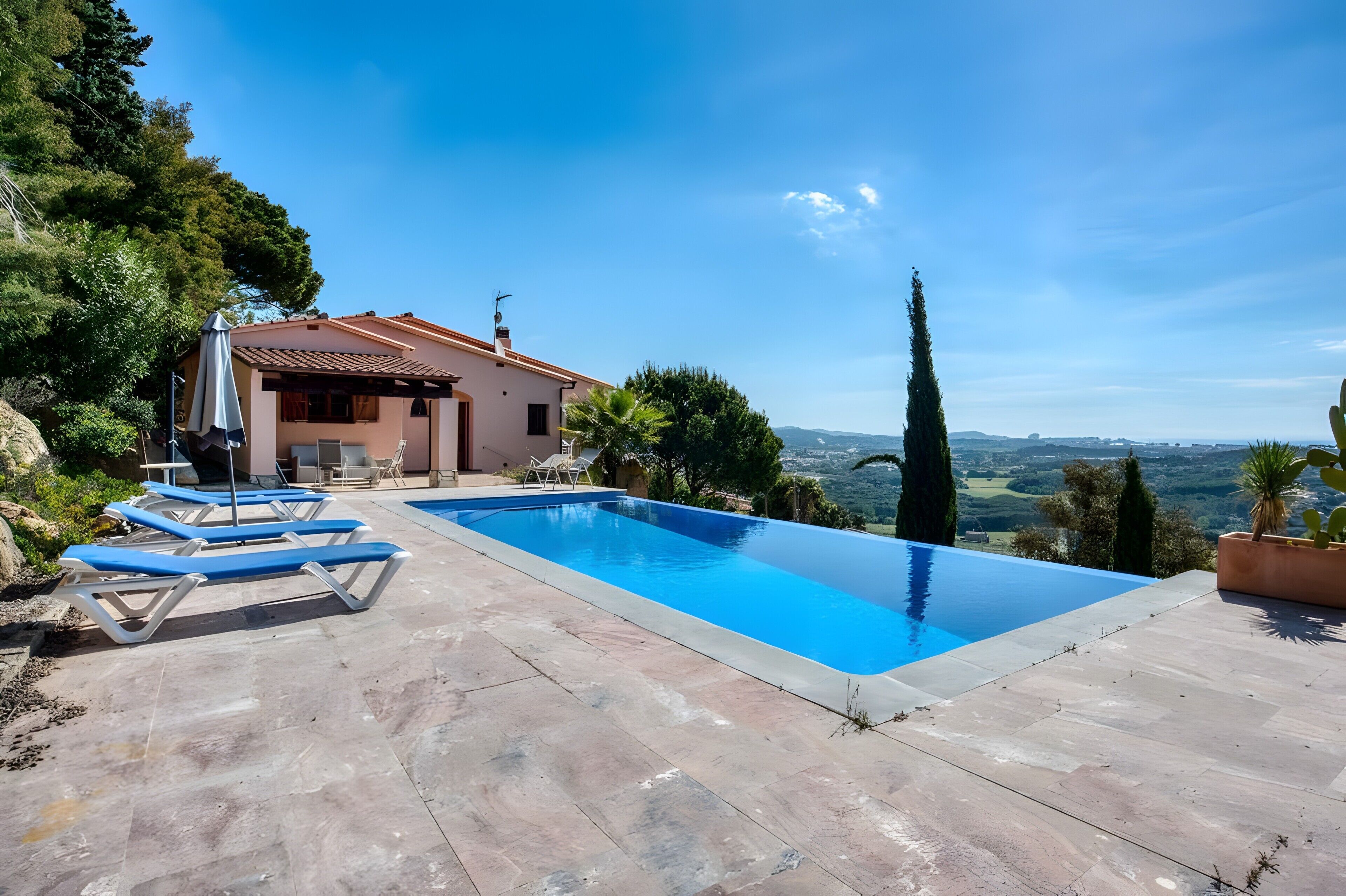 Une piscine avec des chaises longues, une maison avec un toit rouge et une vue sur la campagne.