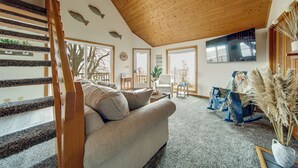 A spacious living area with a wooden staircase, a sofa, a coffee table, and a large window. - Lakeside Living on Wine Trail! Geneva Home w/ Deck (Geneva)