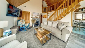 A living room with a sofa, coffee table, wooden staircase, fireplace, and a dining area. - Lakeside Living on Wine Trail! Geneva Home w/ Deck (Geneva)