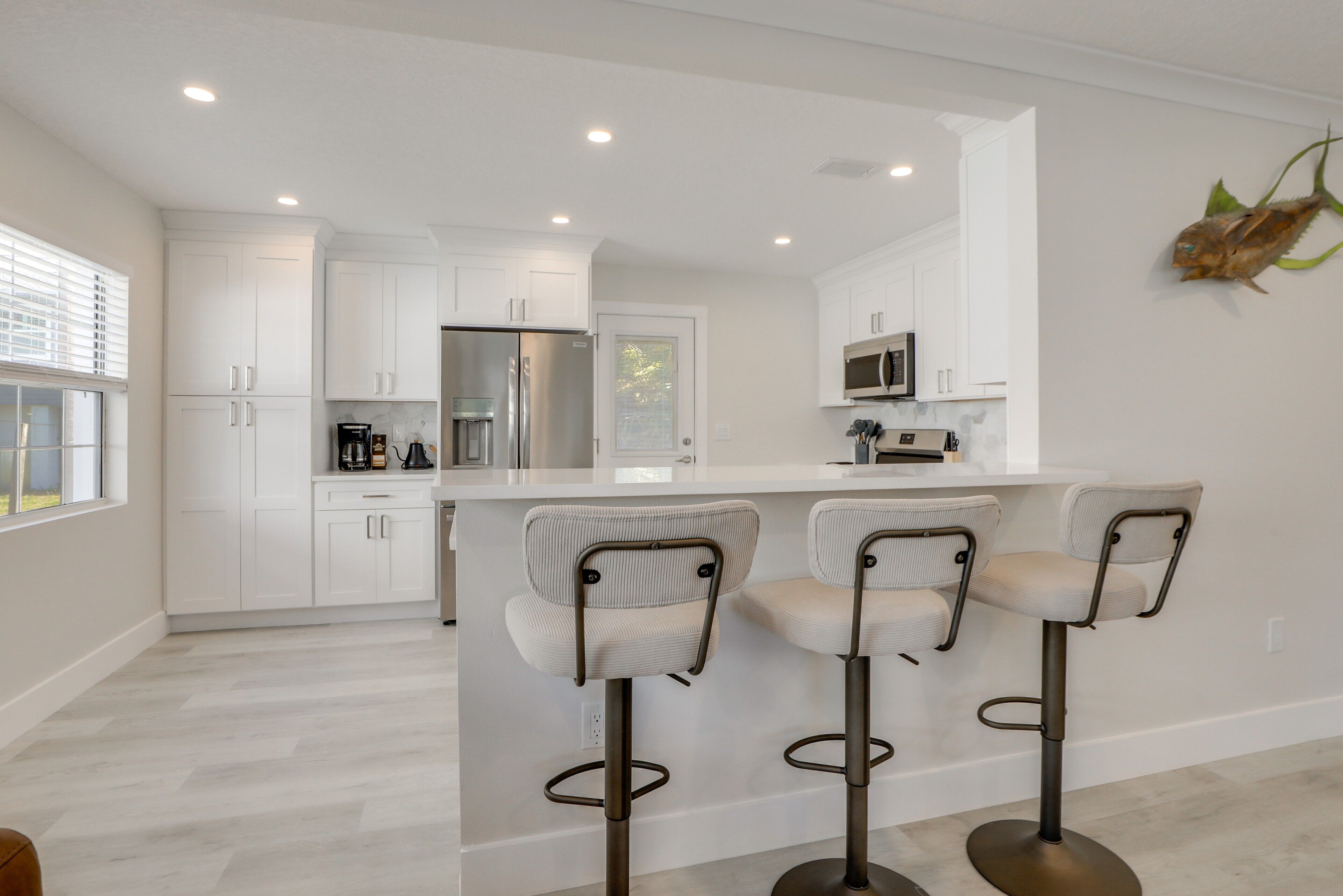 Una cocina moderna con armarios blancos, un refrigerador de acero inoxidable, un microondas y una barra con tres taburetes.