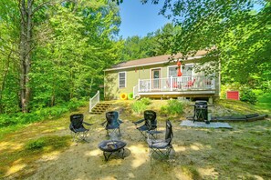 A cabin with a deck, surrounded by trees, and equipped with outdoor seating and a grill.