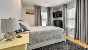 A modern bedroom with a bed, bedside table, lamp, and a mounted TV. - 4 Mi to Hyde Park Village! Modern Escape w/ Yard (Tampa)