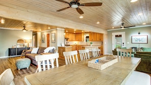 A spacious living room with a large wooden dining table, white chairs, a sofa, and a ceiling fan. - Bring Your Boat! Waterfront Stay on Tims Ford Lake (Estill Springs)