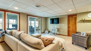 A living room with a sofa, a wicker chair, a television, and a clock on the wall. - Bring Your Boat! Waterfront Stay on Tims Ford Lake (Estill Springs)