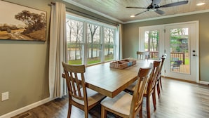 A dining area with a wooden table and chairs, a ceiling fan, and a view through large windows. - Bring Your Boat! Waterfront Stay on Tims Ford Lake (Estill Springs)