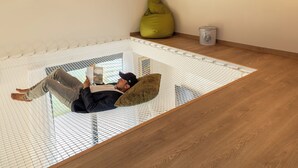 Una habitación con techo inclinado, una hamaca, un sillón de saco y un cubo.