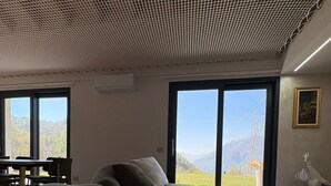 Una habitación con una cama grande, una mesa de comedor y sillas, vistas a montañas a través de amplios ventanales y un techo con diseño de cuadrícula.