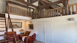 A loft-style room with exposed wooden beams, a staircase, a sofa, a chair, and a painting on the wall. - Charming and comfortable holiday home in Melay (Melay)