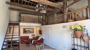 A rustic interior with a wooden staircase, leather sofas, a dining table, and a balcony with wicker baskets. - Charming and comfortable holiday home in Melay (Melay)