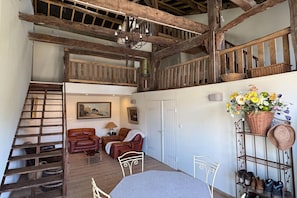 A rustic interior with a wooden staircase, leather sofas, a dining table, and a balcony with wicker baskets. - Charming and comfortable holiday home in Melay (Melay)