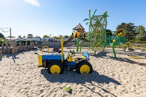 Ein Sandspielplatz mit Traktor, Klettergerüsten und einer Schaukel.