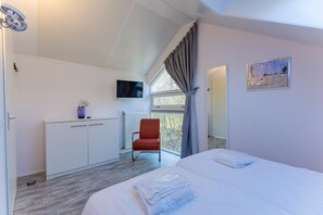 Ein Schlafzimmer mit einem Bett, einem roten Sessel, einem Fernseher und einem Fenster mit Vorhängen.