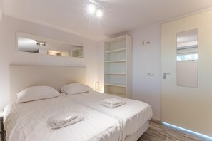 A bedroom with two beds, a built-in shelf unit, a mirror, and a door with a window. - Beachfront Coastal Villa in Renesse for 6 (Renesse)