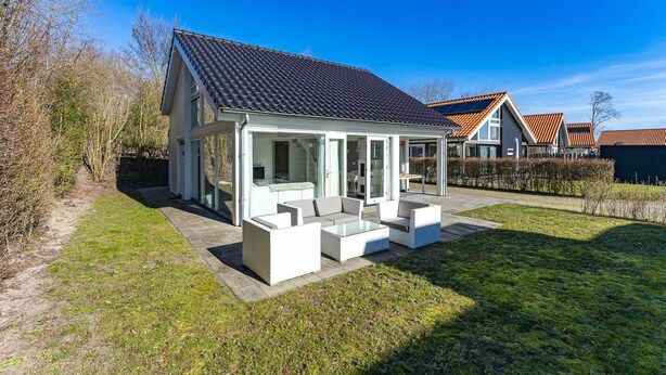 A modern house with a covered patio area, a visible garden, and a clear blue sky. - Beachfront Coastal Villa in Renesse for 6 (Renesse)