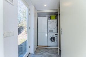 Ein kleiner Waschraum mit Waschmaschine und Trockner, einem Fenster und einer Tür, die nach draußen führt.
