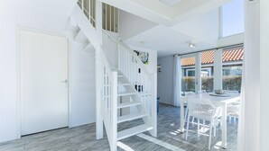 A modern interior with a white staircase, a dining area with white furniture, and a view of the outside. - Beachfront Coastal Villa in Renesse for 6 (Renesse)