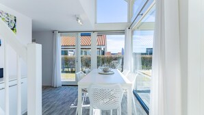 A modern kitchen with a dining area, large windows, and a view of a residential area. - Beachfront Coastal Villa in Renesse for 6 (Renesse)