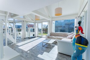 A modern interior with a white sofa, a coffee table, and a colorful sculpture. - Beachfront Coastal Villa in Renesse for 6 (Renesse)