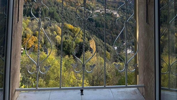 Een balkon met een sierijzeren hekwerk met uitzicht op een bergachtig landschap.