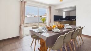 Een eethoek met een tafel voor vier personen, een keuken op de achtergrond en uitzicht op het strand door een schuifdeur.