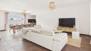 Een moderne woonkamer met een bank, televisie, eethoek en keuken.