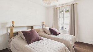 Een slaapkamer met twee bedden, een houten hoofdbord, een hanglamp en een raam met gordijnen.