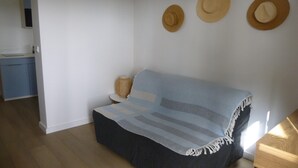 Ett rum med en soffa, ett litet sidobord, en hatt som hänger på väggen och ett köksområde i bakgrunden.