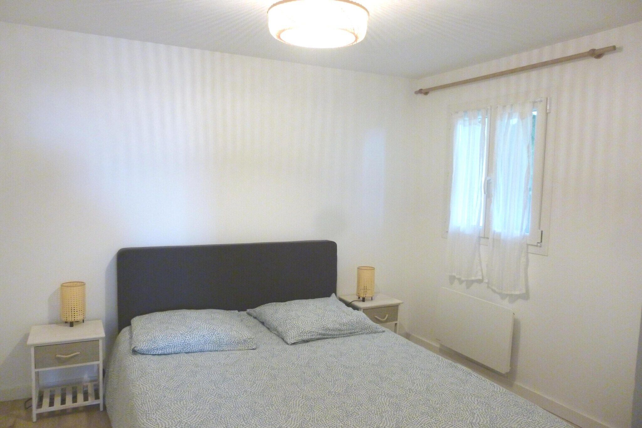 A bedroom with a bed, two bedside tables, a window with curtains, a radiator, and a ceiling light fixture.