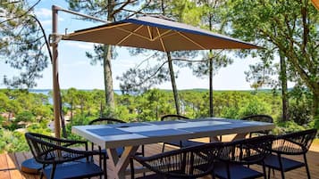 An outdoor deck with a table and chairs, a large umbrella, and a scenic view of trees and water.