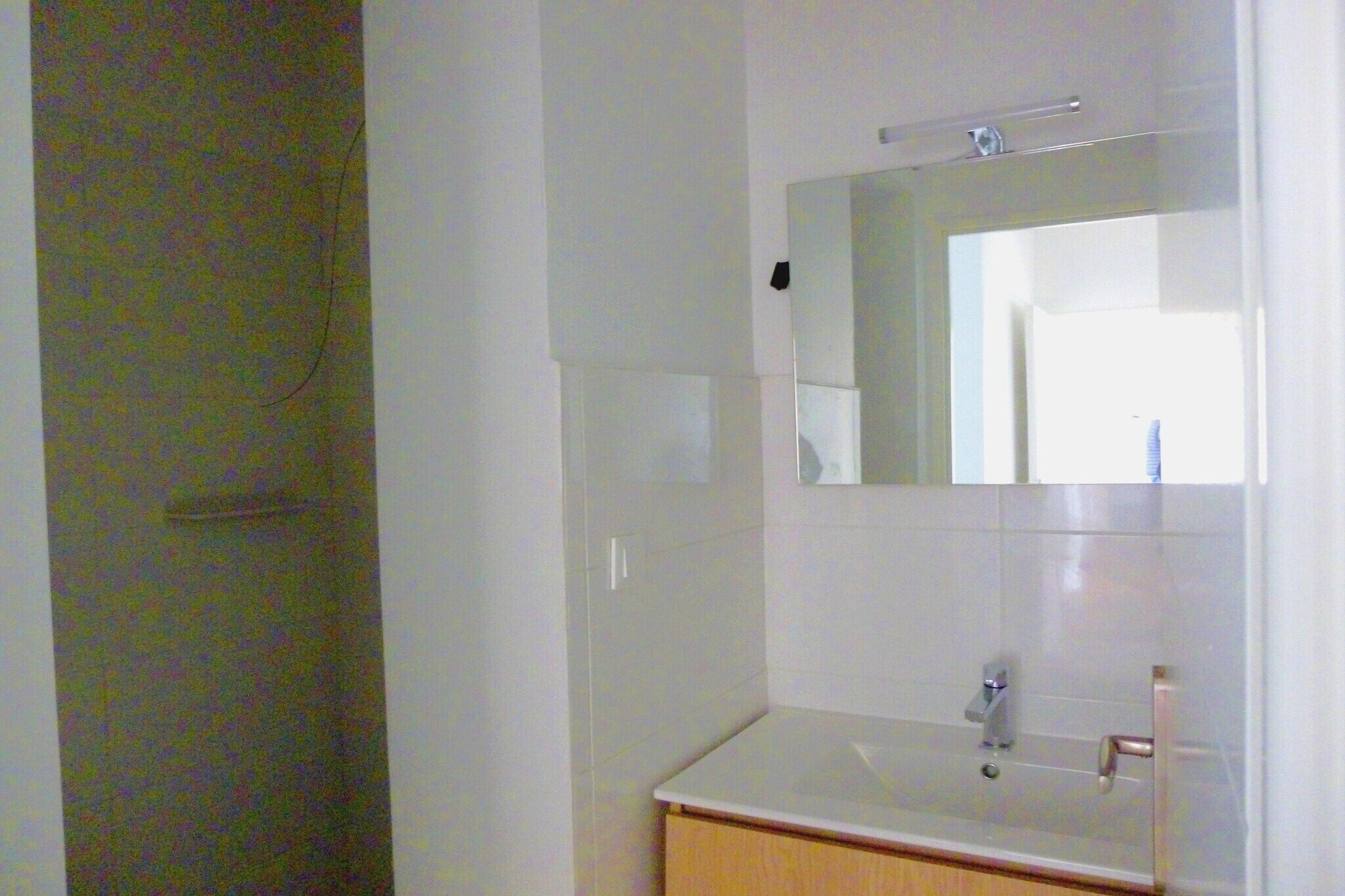 Une salle de bain avec un lavabo blanc, un miroir et une porte.