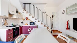 A compact kitchen with a dining area, white cabinets, a microwave, and a staircase. - Holiday home with air conditioning and shared pool (Viddalba)