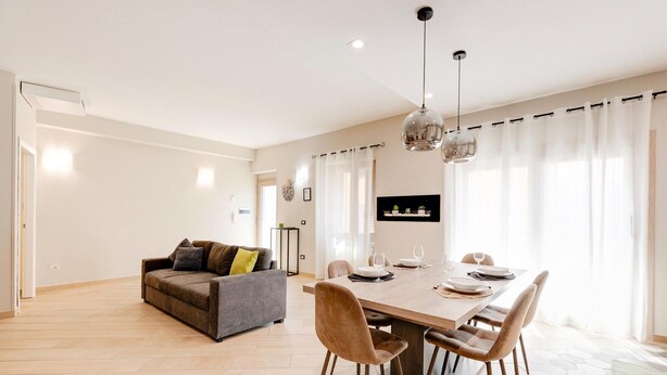 Ein modernes Wohnzimmer mit einer Couch, einem Esstisch, Stühlen und einer Pendelleuchte.