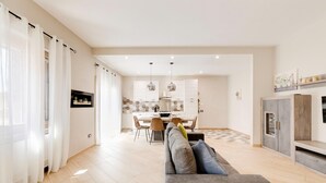 Ein modernes Wohnzimmer mit einem grauen Sofa, einem Essbereich mit Tisch und Stühlen und einer Küche im Hintergrund.