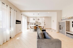 Ein modernes Wohnzimmer mit einem grauen Sofa, einem Essbereich mit Tisch und Stühlen und einer Küche im Hintergrund.